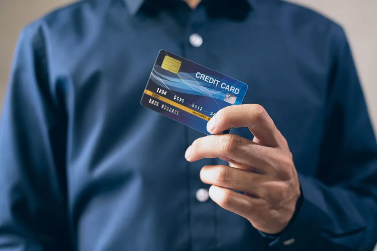 Hand holding a navy bank card at a payment terminal in Dubai with a gold card on the counter
