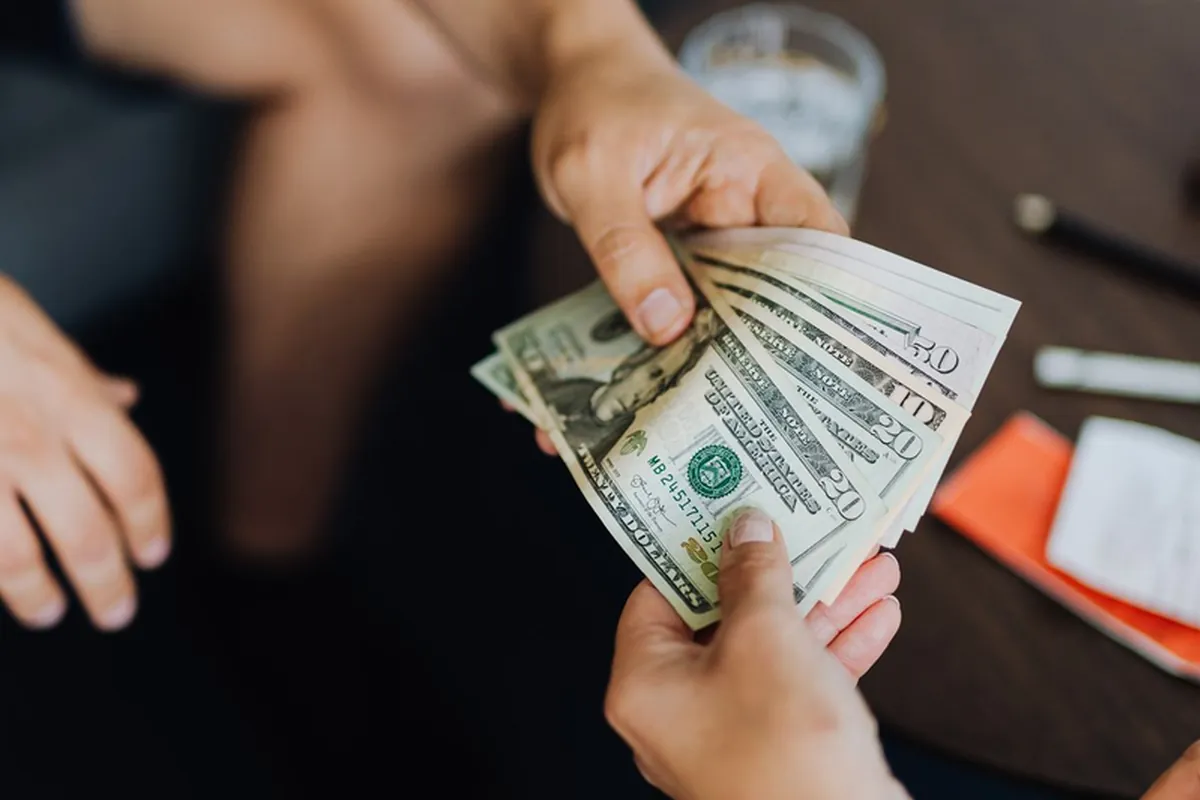 Hands exchanging US dollar bills for remittance transfer