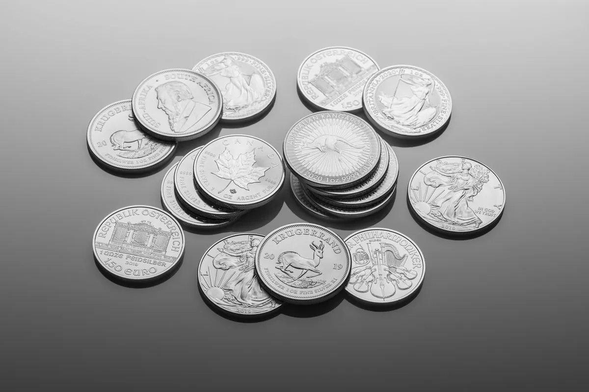 Polished silver bars and coins stacked on dark marble