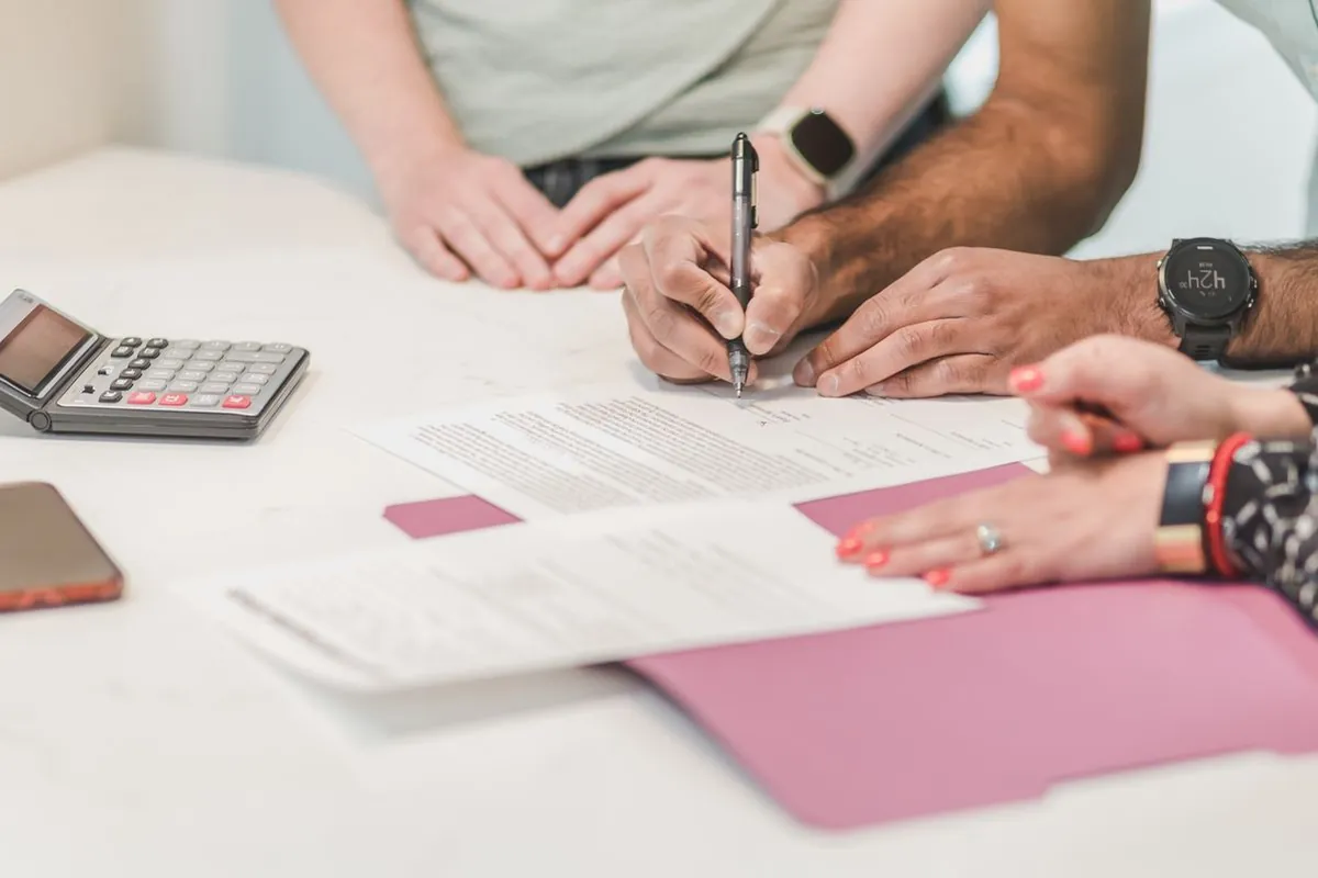 Borrower signing personal loan documents at a bank desk with calculator
