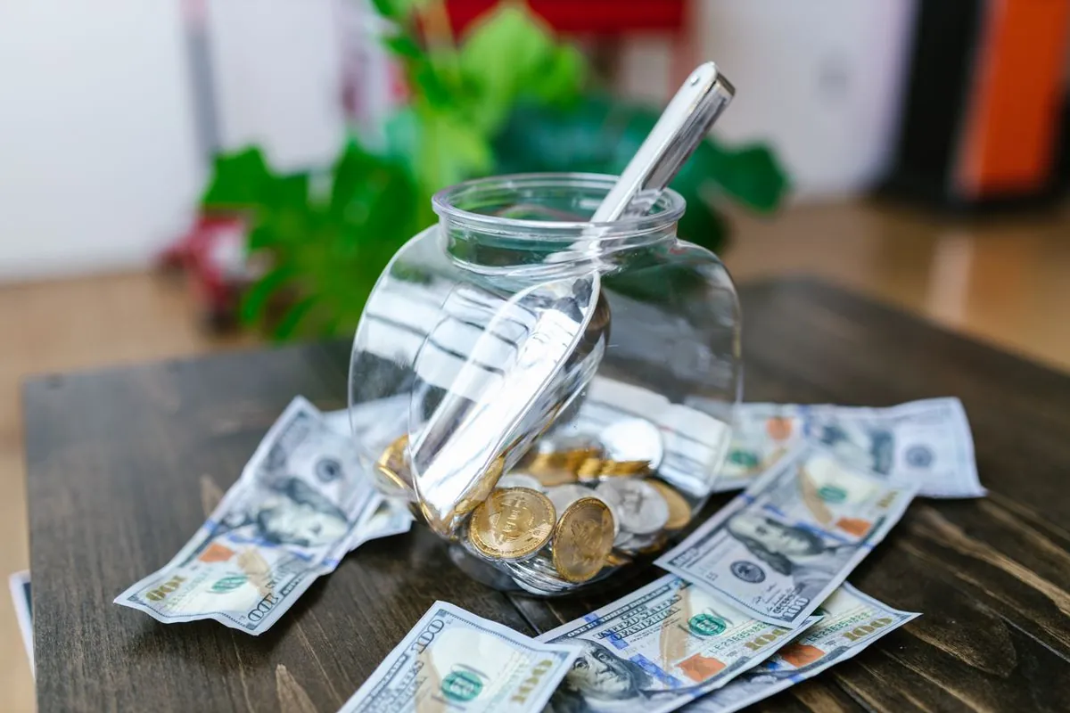 Hand dropping UAE dirham coins into a glass savings jar against the Dubai Marina skyline at sunset
